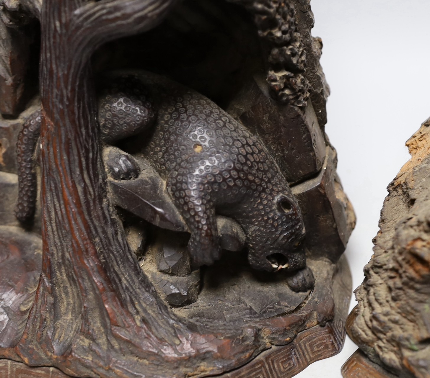 A wood carving of a bear climbing amongst rocks and a tree and another similar carving of figure cooking inside a cave, 40cms high